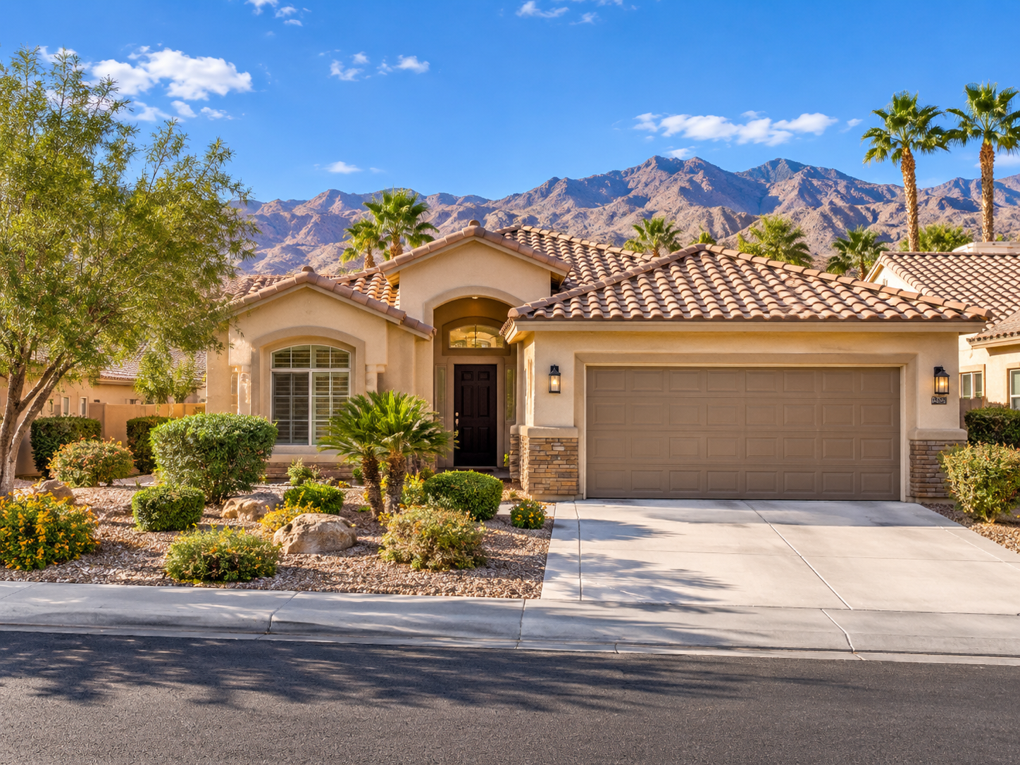 Desert home with tile roof and two-car garage set against rocky mountains under blue sky