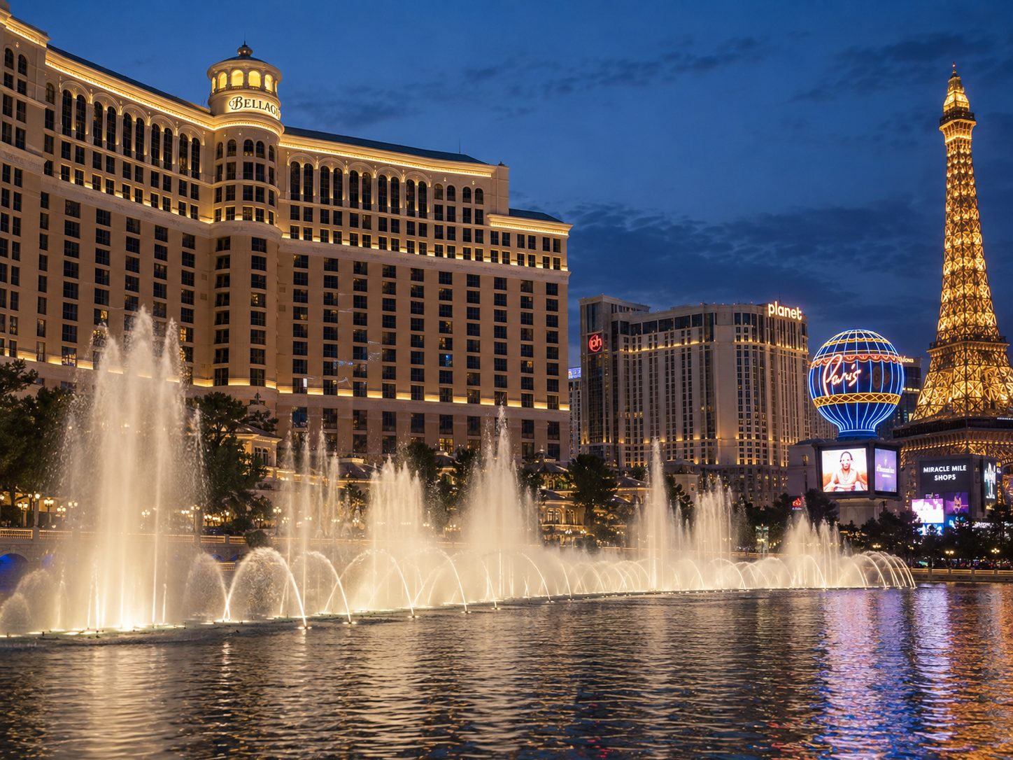 Bellagio fountains illuminated at dusk with Las Vegas Strip skyline and Eiffel Tower replica