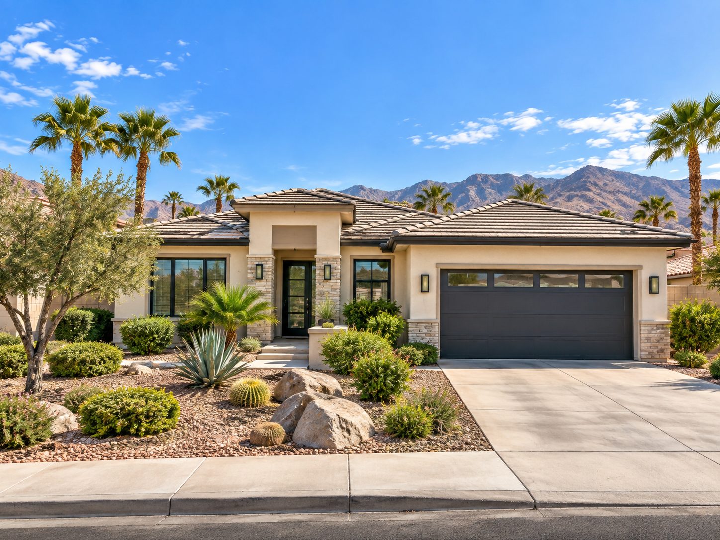 Desert home with tile roof and stone accents backed by rugged mountains under blue sky